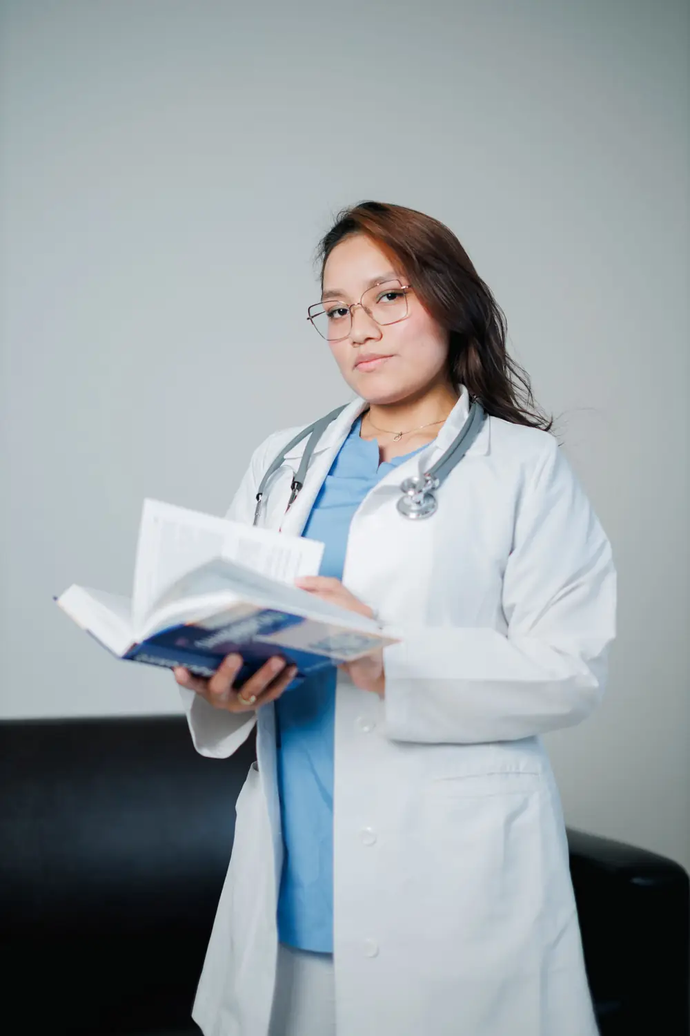 A medical student in a white coat reading an open textbook.